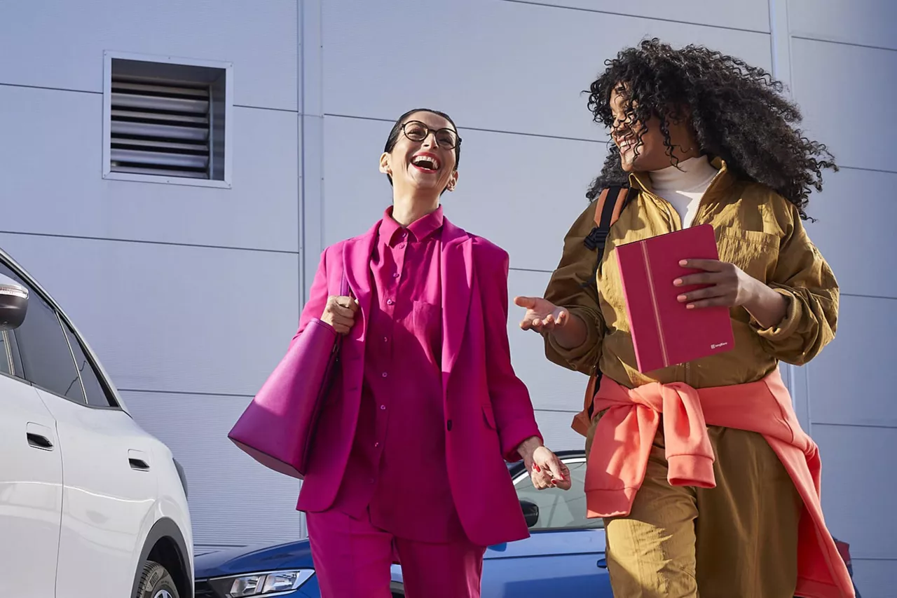 Dos chicas caminando y hablando delante de dos coches
